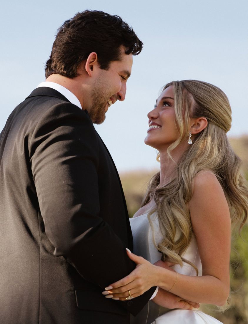 Bride with a sleek half-up style and Hollywood waves looking at her groom